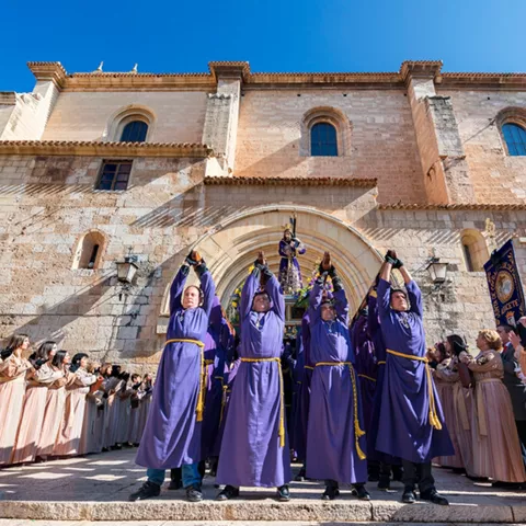 Grupo de penitentes alzando un paso frente a fachada histórica.