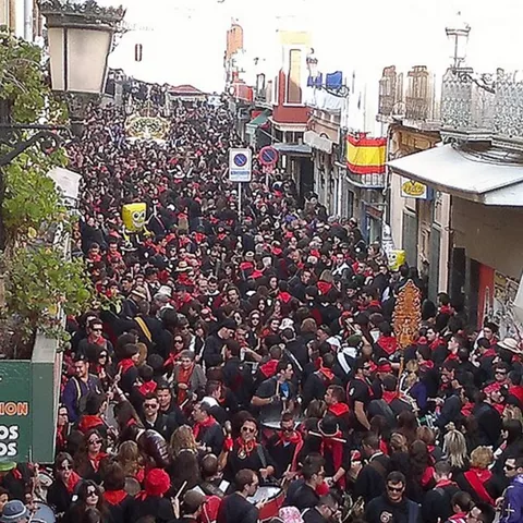 Multitud abarrotando una calle durante una celebración popular con vestimenta oscura y pañuelos rojos.