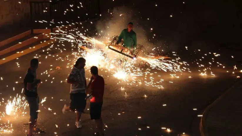 Hombre portando estructura pirotécnica con chispas en la vía pública.