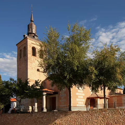 Iglesia de ladrillo visto con una torre campanario robusta rematada por un chapitel oscuro.