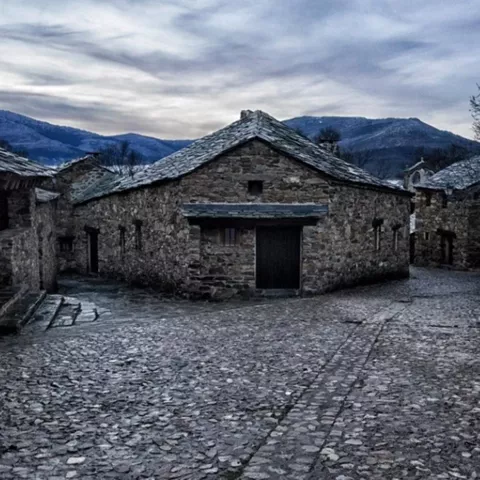 Calle empedrada entre casas de piedra con tejados de pizarra al atardecer.