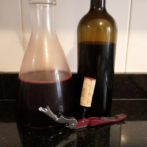Botella y decantador con vino tinto sobre encimera, junto a un sacacorchos.