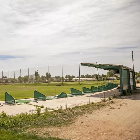 Zona de prácticas de golf con puestos cubiertos y red de seguridad