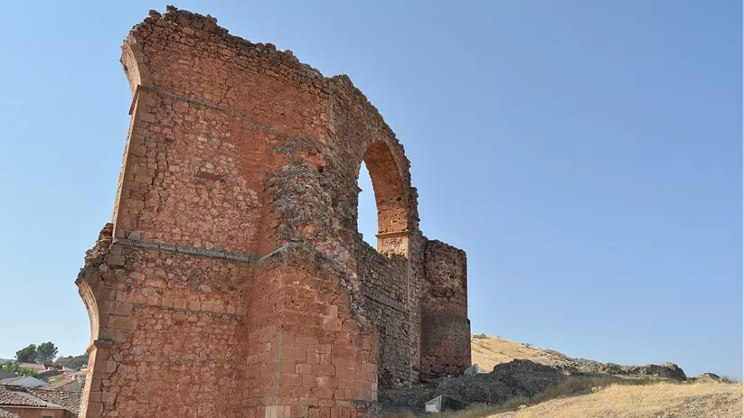 Vista lateral de restos arquitectónicos de piedra con arco elevado sobre terreno inclinado.