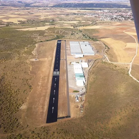 Vista desde el aire de pista recta con marcas de aterrizaje y edificios anexos.