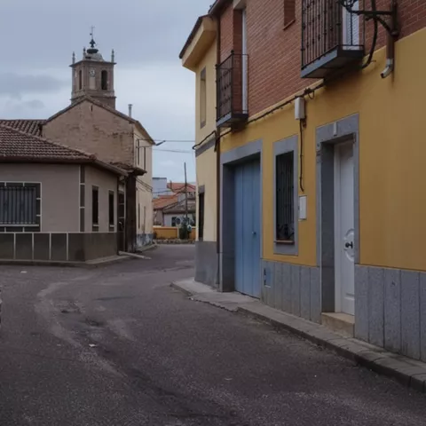 Calle estrecha con viviendas tradicionales y torre al fondo.