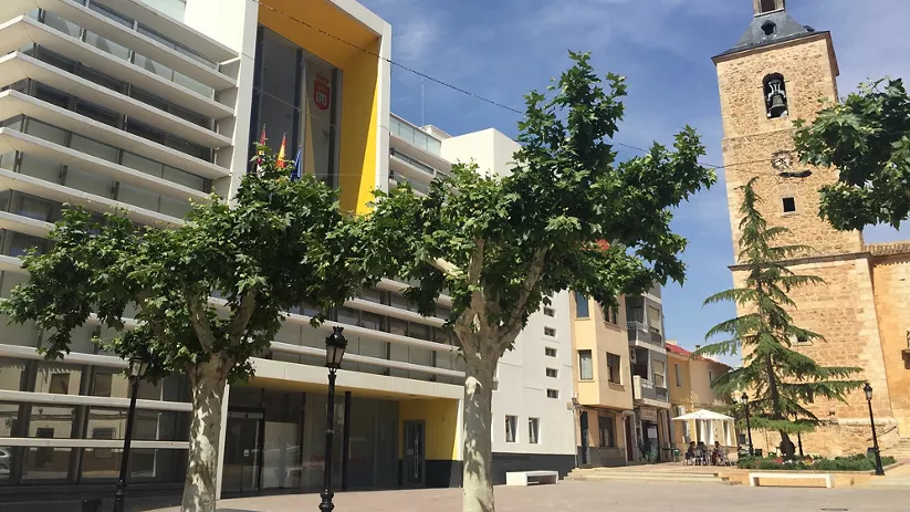 Plaza con edificio institucional moderno y torre histórica al fondo