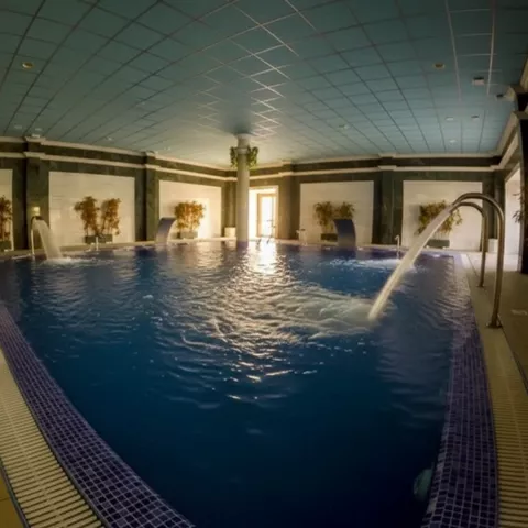 Piscina interior con cascada de agua y luz tenue, rodeada de paredes de mármol.