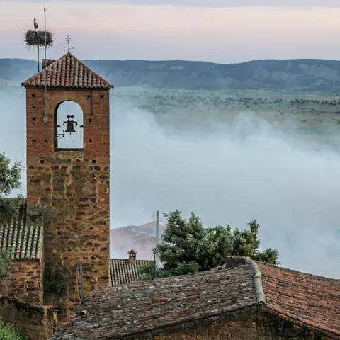 Torre de piedra sobresaliendo entre tejados y bruma matinal
