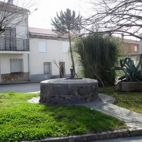 Fuente tradicional de piedra en una plaza ajardinada.