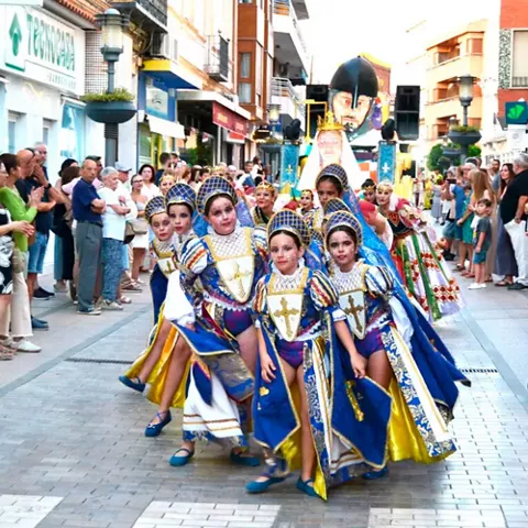 Desfile infantil con trajes coloridos y público a ambos lados de la calle