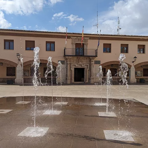 Plaza porticada con fuentes y edificio institucional.