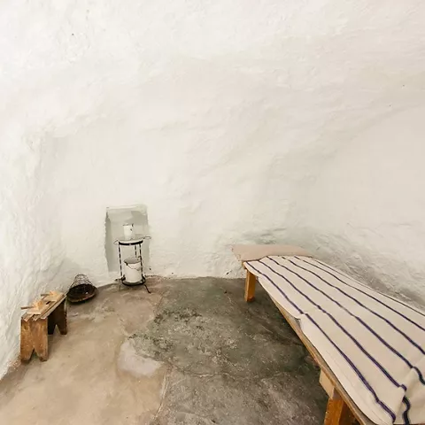 Estancia subterránea con cama sencilla y muros encalados