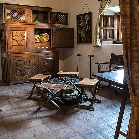 Sala con mobiliario antiguo de madera, vigas vistas y pequeña mesa con taburetes.