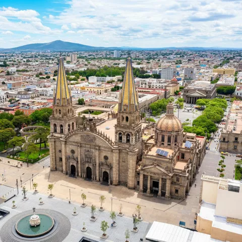 Vista aérea de catedral con torres y plaza arbolada.