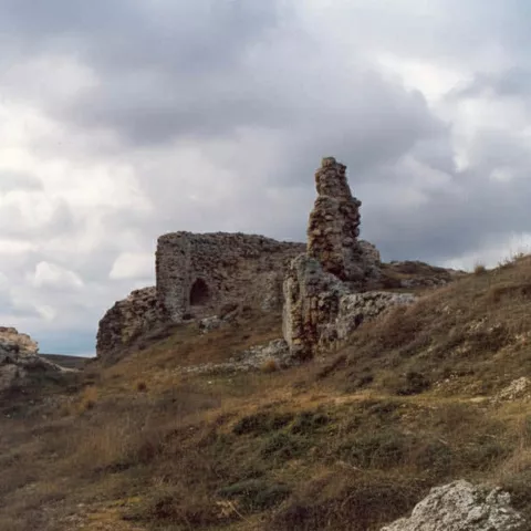 Estructura defensiva en ruinas sobre ladera verde.