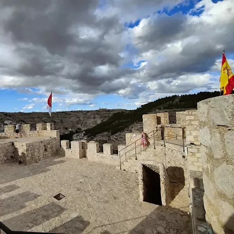 Interior de muralla con almenas, escaleras de piedra y banderas ondeando.