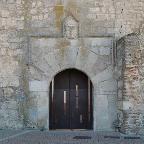 Puerta de arco de piedra con gran portón oscuro en muro antiguo.