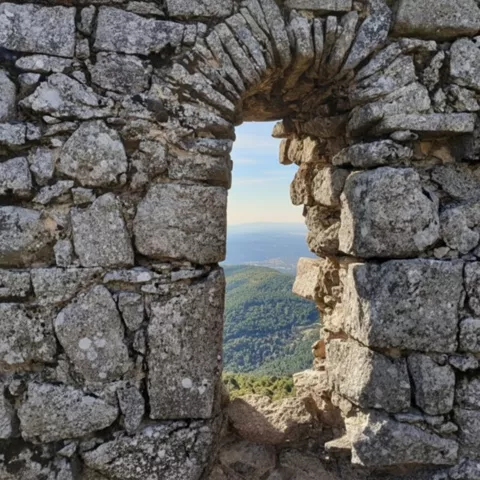 Ventana de piedra en muro antiguo con paisaje montañoso al fondo.