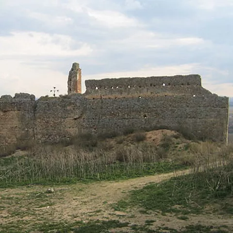 Vista lateral de una fortaleza en ruinas con campos abiertos al fondo.