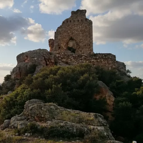 Ruinas de fortaleza sobre colina rocosa al atardecer.