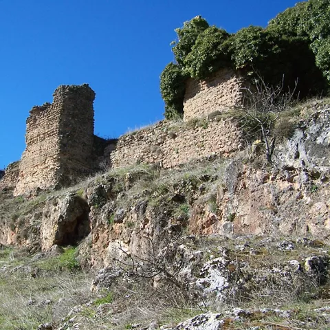 Restos de muralla de piedra sobre un cerro con sendero y vegetación.