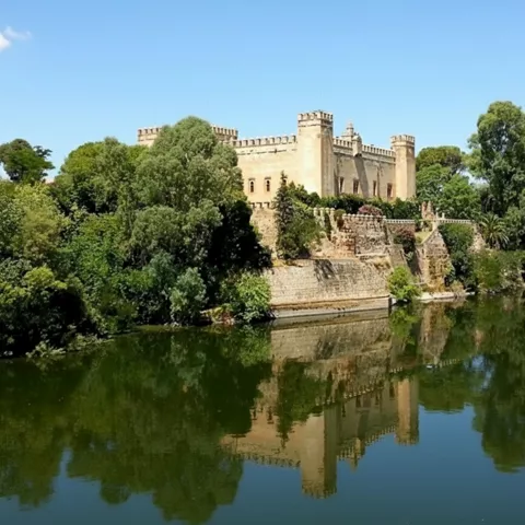 Fortaleza histórica reflejada en un río rodeado de vegetación