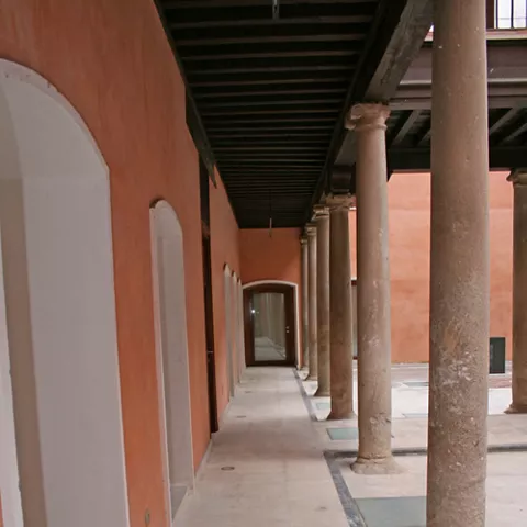 Galería porticada con columnas de piedra y suelo de mármol.