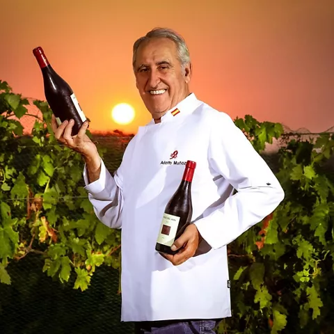 Cocinero con dos botellas de vino al atardecer entre viñas