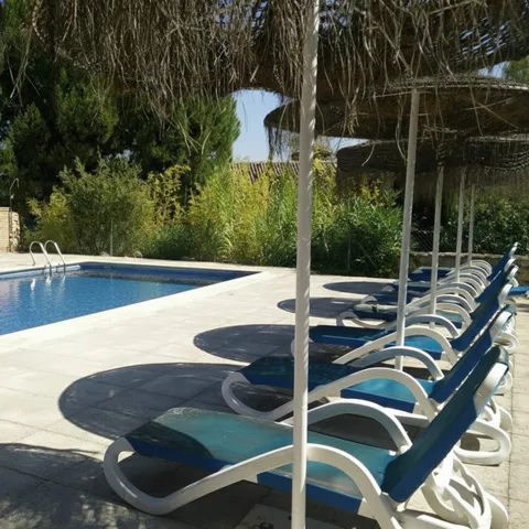 Piscina exterior con tumbonas bajo sombrillas de mimbre.