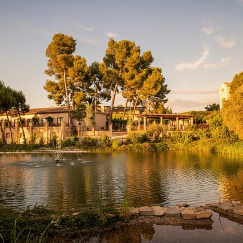 Lago con fuente y edificio rodeado de árboles al atardecer.