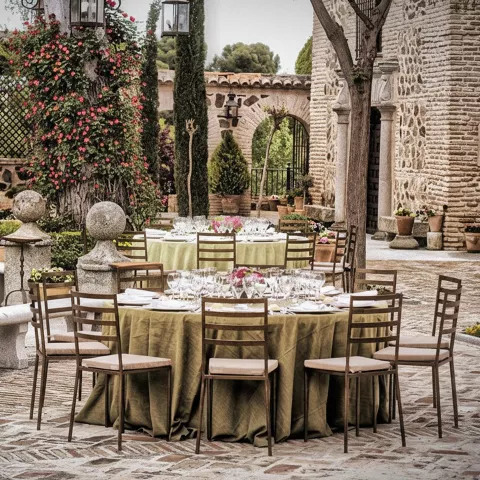 Mesa redonda montada en patio de piedra con flores y faroles.