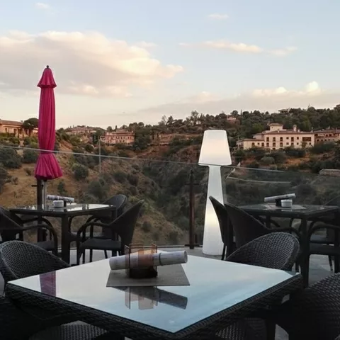 Terraza con mesas, sombrillas cerradas y vistas a la ladera.