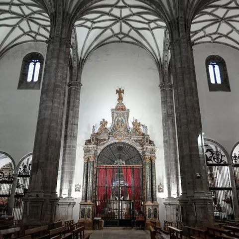 Capilla lateral con reja, cortinajes rojos y bóvedas de crucería