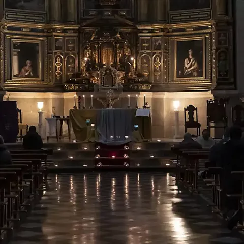 Interior de iglesia con altar iluminado y fieles sentados en los bancos.