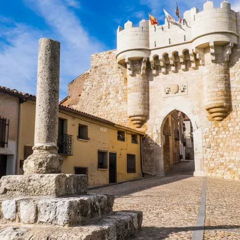 Puerta fortificada junto a columna de piedra en plaza.