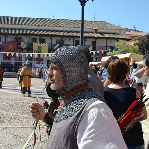 Escena de recreación medieval en una plaza con figurantes armados y público alrededor.