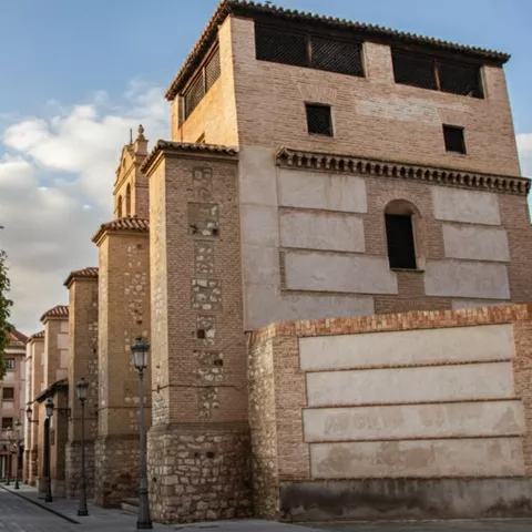 Fachada lateral de edificio histórico de ladrillo y piedra en calle tranquila.