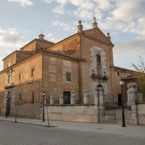 Vista lateral de iglesia de ladrillo con portada escultórica y verja perimetral.