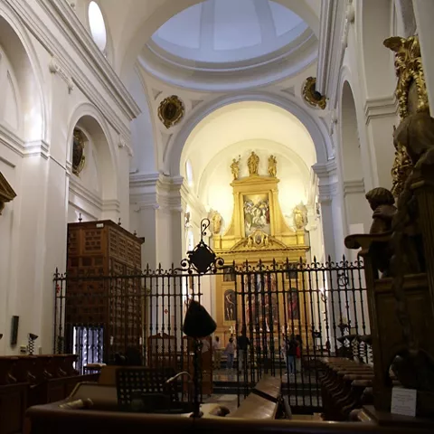 Interior de iglesia con nave alta, reja de hierro y retablo dorado al fondo.