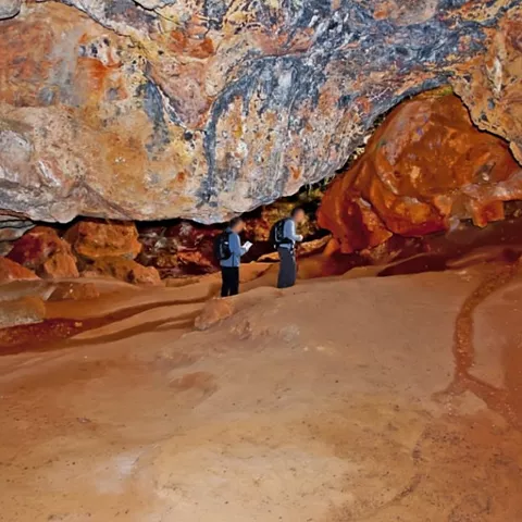 Visitantes explorando el interior de una cueva con formaciones anaranjadas.