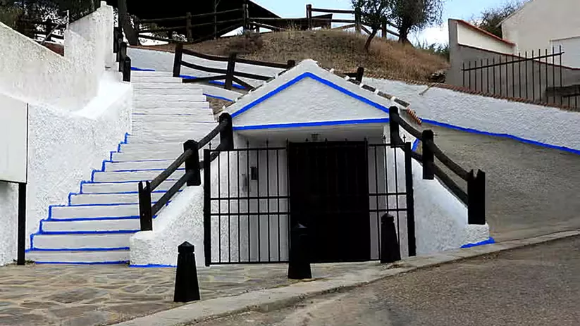 Entrada subterránea encalada con escaleras laterales y barandillas de madera.