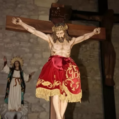 Imagen de Cristo crucificado con paño rojo y flores en el altar.
