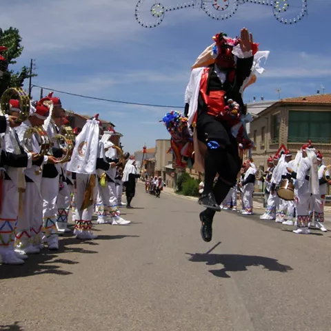 Danza popular en la calle con músicos y participantes con trajes festivos.