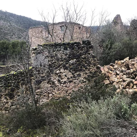 Restos de edificaciones de piedra entre matorral y colinas