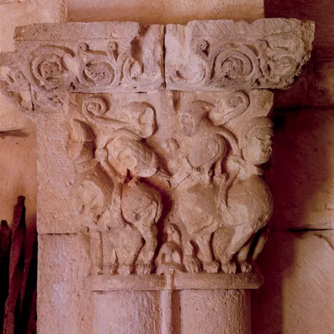 Capitel tallado en piedra con figuras animales enfrentadas.