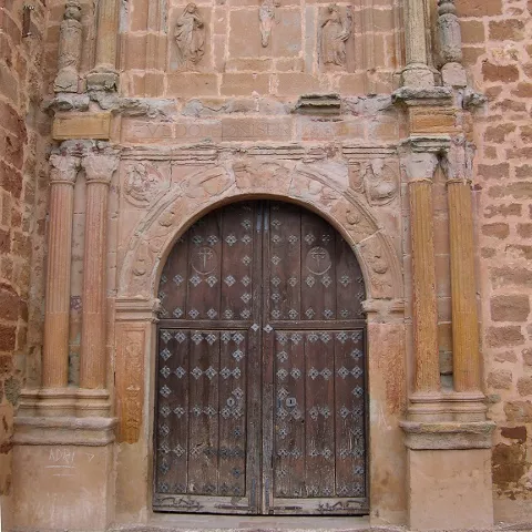 Puerta de madera con arco y relieves en piedra.
