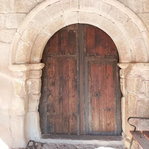 Puerta de madera bajo arco románico tallado.