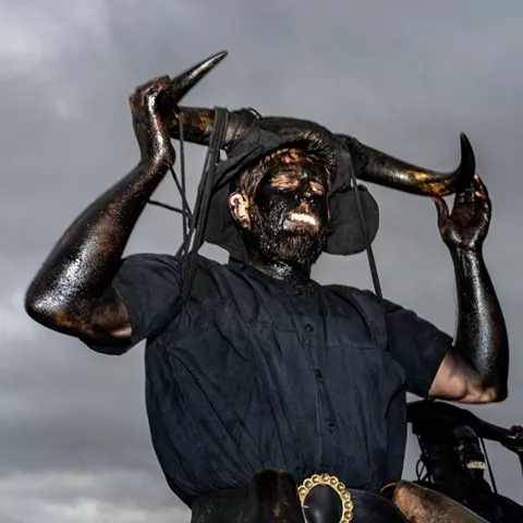 Hombre con cuernos levantados sobre fondo oscuro.
