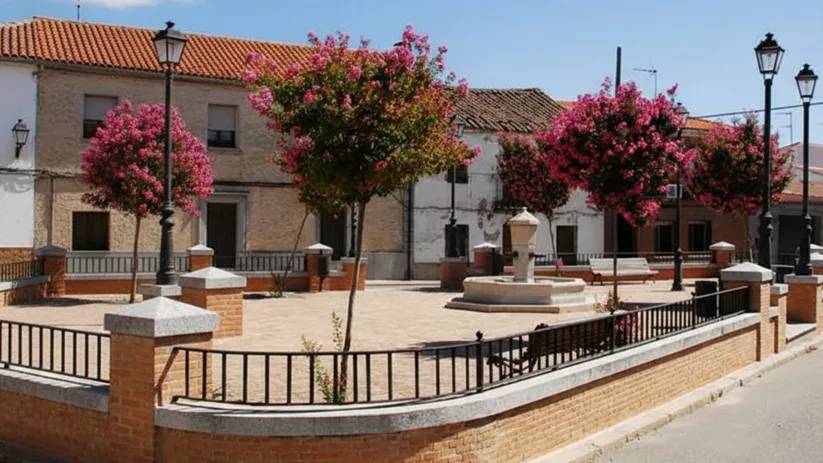 Plaza ajardinada con fuente, rodeada de viviendas tradicionales y árboles en flor.